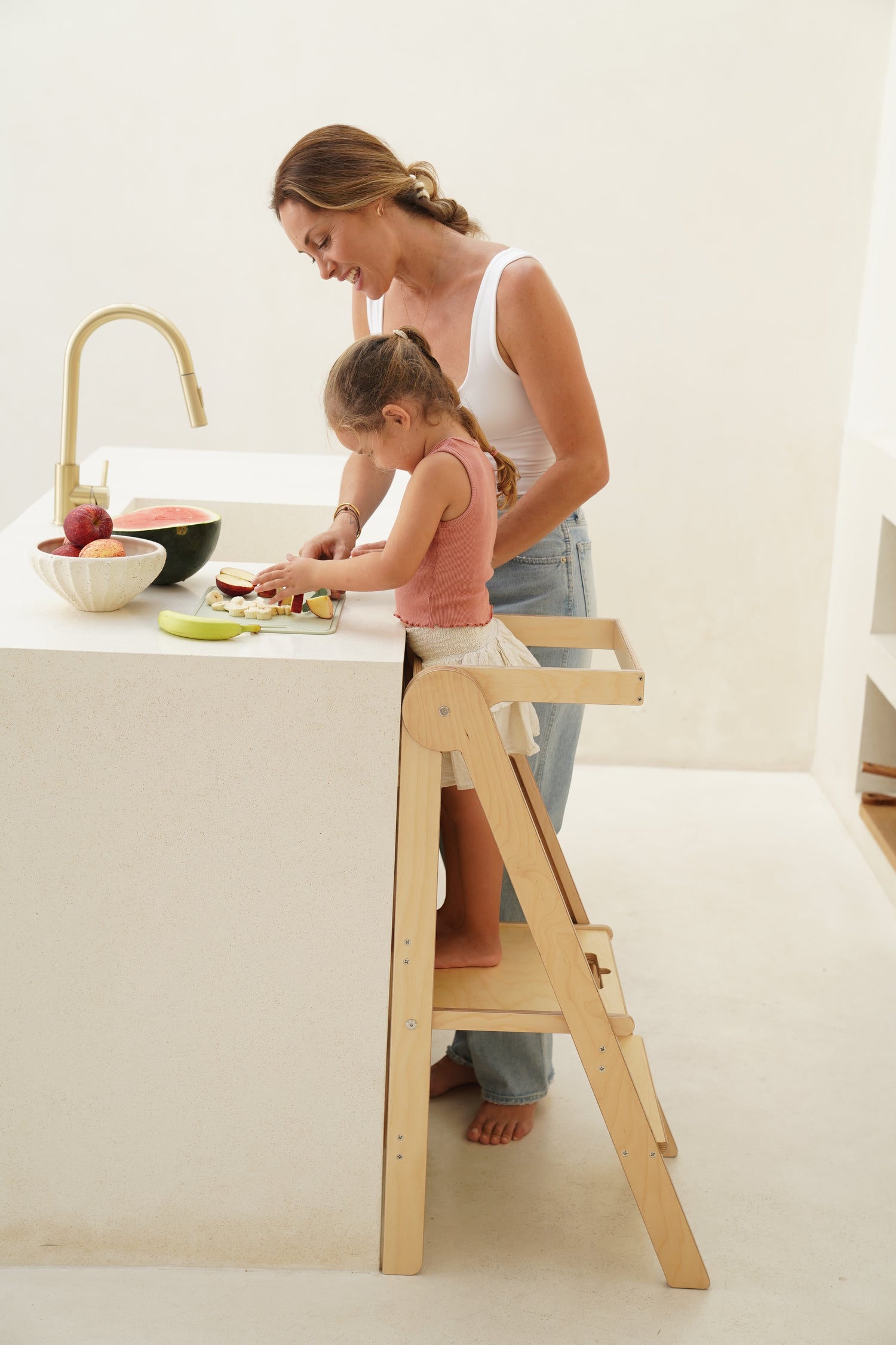 Child cooking with parent in the kitchen, preparing fruit salad
